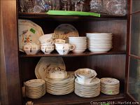 Shelf with stacked cups, saucers, and plates showing floral and bird pattern on white china.