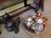 Photo of the entire lot showing stoneware tea pot set (4 pieces), pewter tea pot set with wooden handles, copper-colored handleless cups, mini pitcher and metal tray.