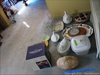 View of serving ware items laid on floor including covered ceramic pieces, platter, wooden cheese server, clear glass trifle bowl in box