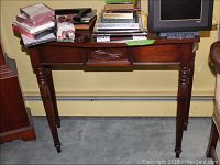 Full view of the vintage console table showing carved tapered legs, carved apron and dark wood finish with items on top.