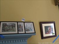 Three Lionel Barrymore metal etching prints: two boat scenes and one farm scene, framed on wall above a blue mantelpiece.