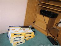 Seven packs of Hammermill printer paper stacked on floor next to wooden office desk shelf with black printer above