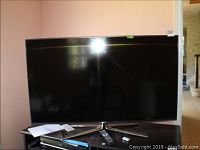 Samsung 50 inch flat panel TV with remote and batteries on wooden surface, screen off, with reflection glare