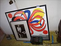 Photo showing framed Alexander Calder poster behind acrylic, framed matted black and white Chris Evert tennis photo standing in front, and the three VHS tapes stacked on carpeted floor.