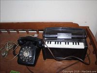 Photo showing both the black rotary telephone and the black vinyl Magnus electric organ together on a wooden surface.