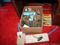 Box of vintage Marklin train track pieces, one train car, and 1975 Marklin catalog on red carpet