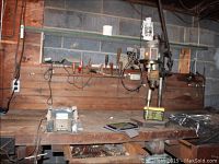 Workbench with vintage drill press and assorted hand tools on the surface and shelf, showing workspace and tools' environment.