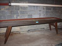Full view of the vintage shuffleboard table showing tapered legs, wooden frame and clear top surface with some dirt and dust.