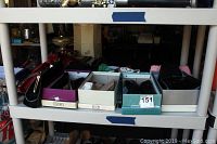 Shelf view of various women's purses, shoes in boxes, and other accessories stacked on a white shelf.
