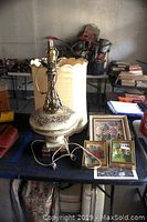 Vintage table lamp with tattered cream fabric shade and floral base, assorted picture frames with floral artwork laid on a table.