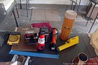 Photo showing two vintage cameras, three flashlights, and an orange cylindrical container on a black table in a garage setting.