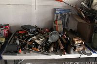 Wide view of assorted vintage hand tools piled on white surface including wrenches, screwdrivers, hammers, pliers, funnels, and various metal tools.