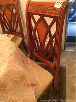 Side view of a wooden dining chair showing the intricate carved backrest pattern and seat cushion with protective plastic cover.