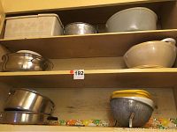 Wooden shelves holding various metal and ceramic pots, a metal pan, metal colander, and plastic bowls.