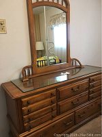 Front view of wood dresser with attached large mirror, showing glass top, drawer handles, and mirror's decorative wooden frame.