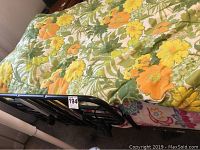 Close-up photo of the bed frame side showing black metal rails and floral bedspread with yellow and orange flowers.