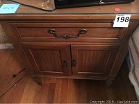Front view of wooden nightstand showing drawer with brass-tone handle and two-door cabinet with brass knobs.