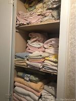 Full view of shelves containing folded towels and linens in pastel shades, stacked in three layers.