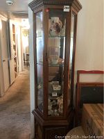 Full view of tall corner wooden display cabinet with glass panels showing inside items