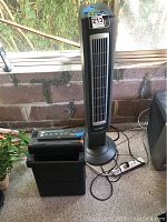 Lasko black tower fan next to Achiever paper shredder on floor near window