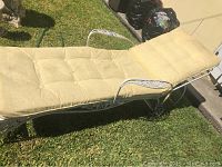 Full view of the white metal lounge chair with beige tufted cushioned upholstery placed outdoors on grass