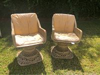 Two matching outdoor swivel chairs with beige cushions placed on grass, showing overall condition and design.