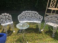White cast iron settee, two matching chairs, and round glass top side table on grass outdoors