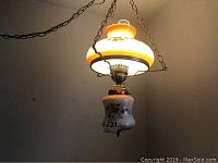Side view of the hanging swag lamp showing the orange and white opaque glass shade adorned with detailed floral patterns and the metal chains suspending it.