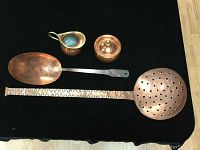 All four copper kitchen items laid out including creamer, sugar bowl with lid, large spoon, and pasta ladle