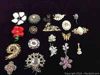 Full view of all 20 brooches arranged on black felt background showing the variety of designs and colors