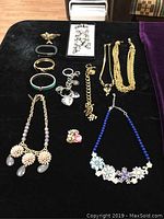 Photo of the entire collection of costume jewelry laid out on black fabric including necklaces, bracelets, a key chain, and a brooch