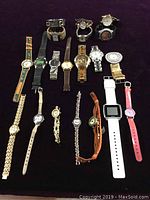 Overview of 20 assorted quartz wristwatches laid out on black background showing various band types and colors including leather, metal, and plastic.
