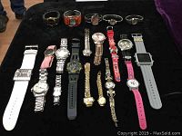 Photo of 20 assorted quartz watches in various styles, bands, and colors laid out on a black surface.