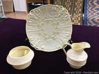 Photo showing Belleek plate, cream pitcher, and sugar bowl on dark fabric