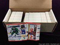 A box filled with neatly stacked 1990 Score NHL hockey cards, visible cards include Alf Sandelinsson.
