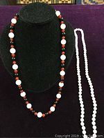 Two bead necklaces displayed on black and purple background; one necklace made of round rose quartz beads, the other featuring alternating carnelian, onyx, and white beads.