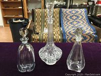 Three crystal decanters on a dark purple cloth with patterned rugs in background; variety of shapes visible