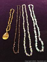 Four necklaces laid flat on a purple cloth background showing distinct bead types and pendant on tiger's eye necklace.