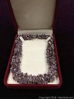 Amethyst necklace neatly placed inside a white cushioned red velvet jewelry box showing the full length of the necklace and clasp.