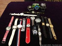 Photo shows 20 assorted quartz wristwatches arranged on table with different band styles and colors