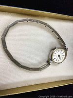 Front view of ladies Seiko solar watch with silver-tone dial and linked metal band laid flat in box.