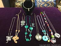 Lot of 10 different necklaces shown on purple cloth, various colors and designs.