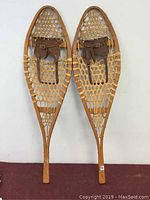 Full view of the pair of wooden snowshoes with leather straps, showing length and design.