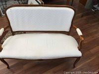 Front view of white upholstered vintage settee with wooden frame and curved legs and arms.