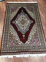 Full view of the rectangular handmade wool rug laid flat on a wooden floor showing medallion and floral design with white fringes.