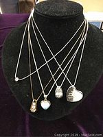 Front view of five sterling silver necklaces on black display stand showing all pendants and chains.