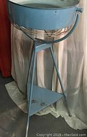 Full height view of blue metal fan stand with triangular base and slightly worn paint.