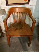 Front view of the vintage solid oak office chair showing the curved back with vertical slats and wooden seat with wear.