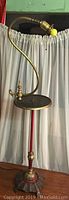 Full view of antique floor lamp showing curved brass neck, brass tray table, and red stand.
