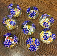 Eight clear glass paperweights with blue floral designs and colorful internal glass swirls, arranged on a wooden surface.